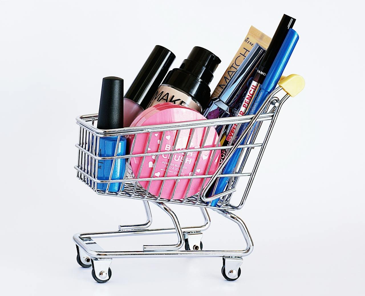our-services-2 Miniature shopping cart filled with a variety of cosmetics on a white background.